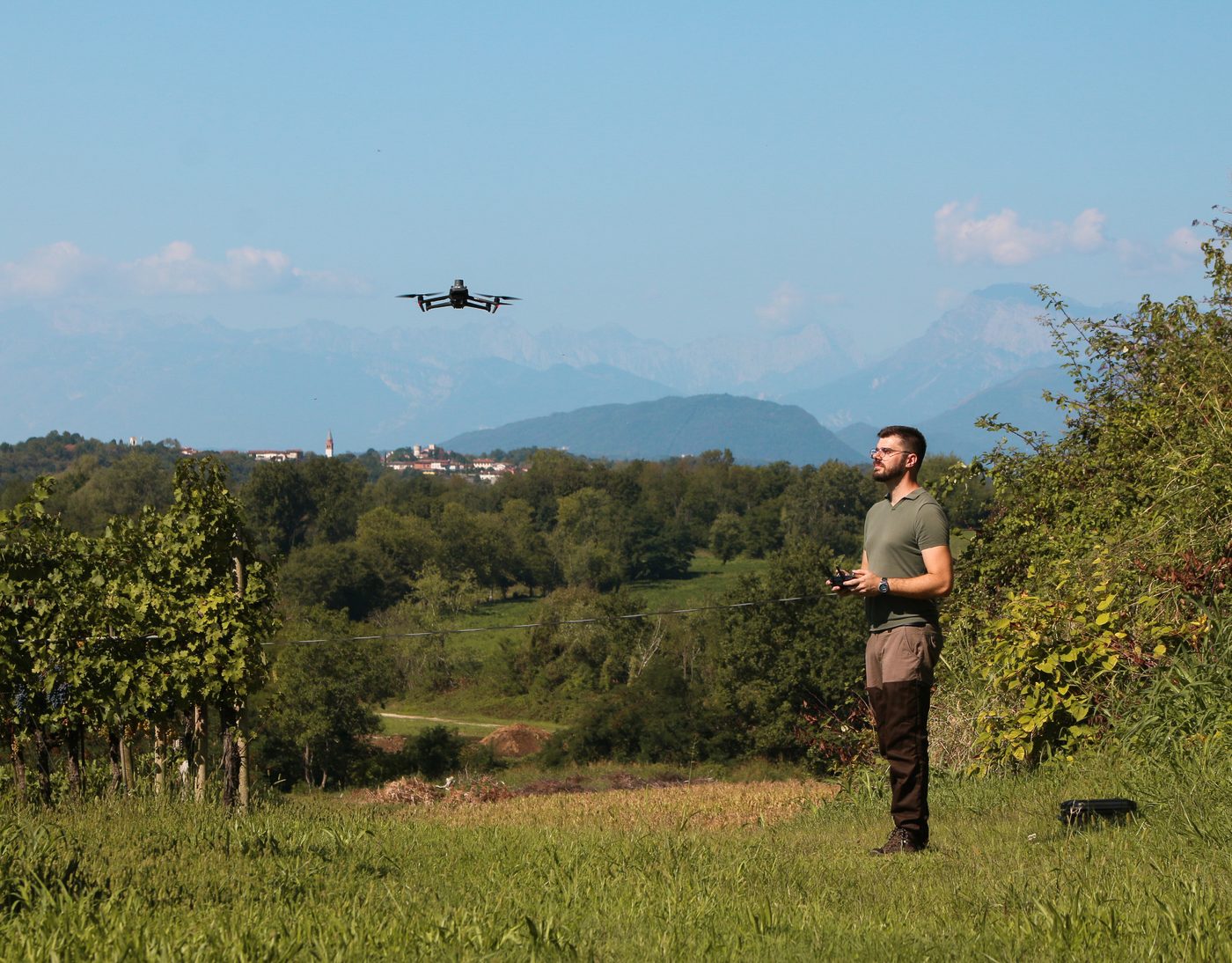 Fabio Plaino nel vigneto mentre pilota il drone, con le montagne del Friuli sullo sfondo